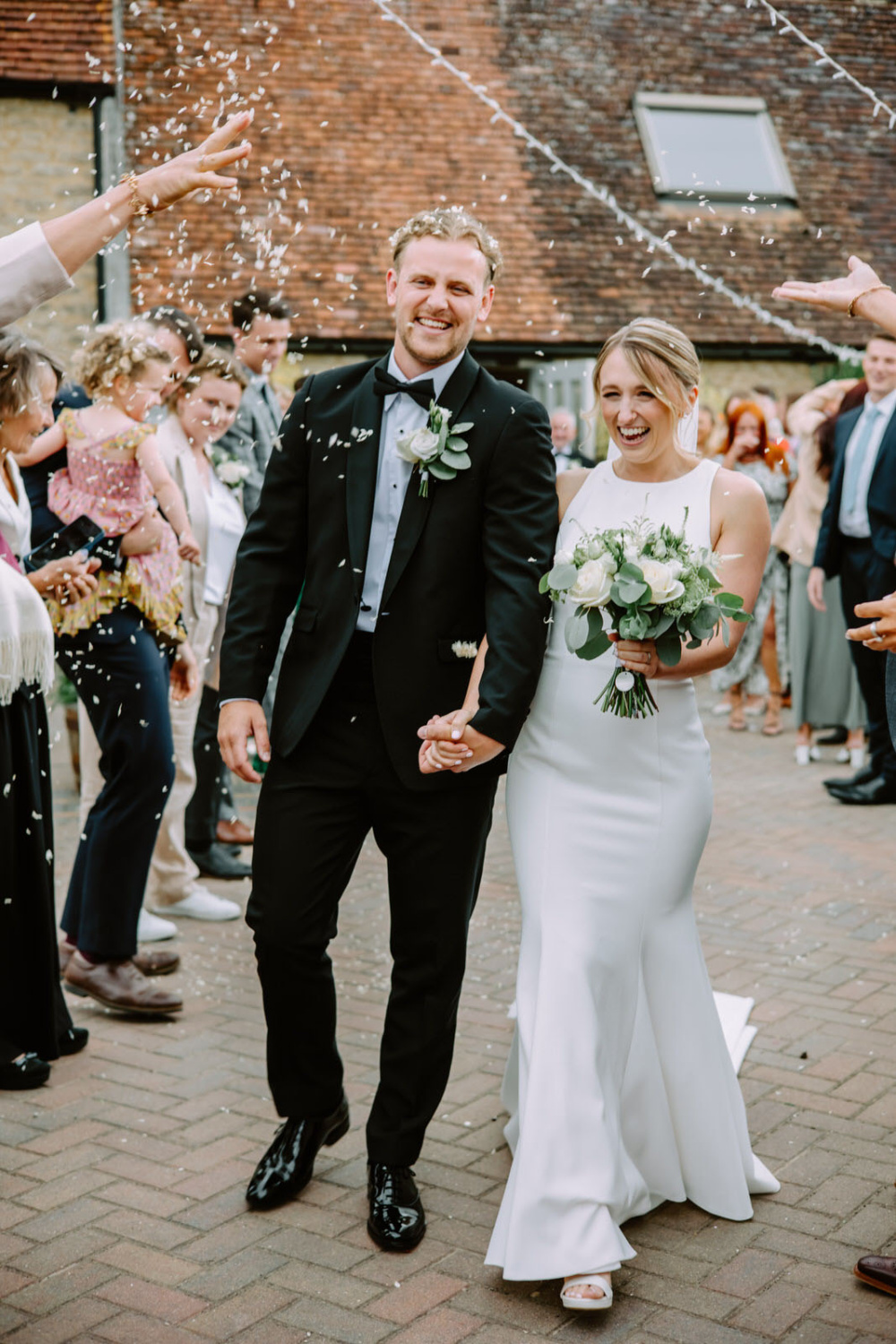 A bride and groom walking down the aisle with confetti thrown at them at tha front of the Stratton court Barn at their wedding.