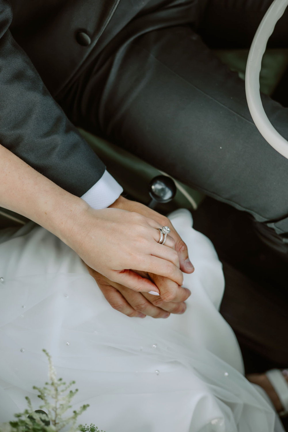 A bride and groom holding hands in a car.