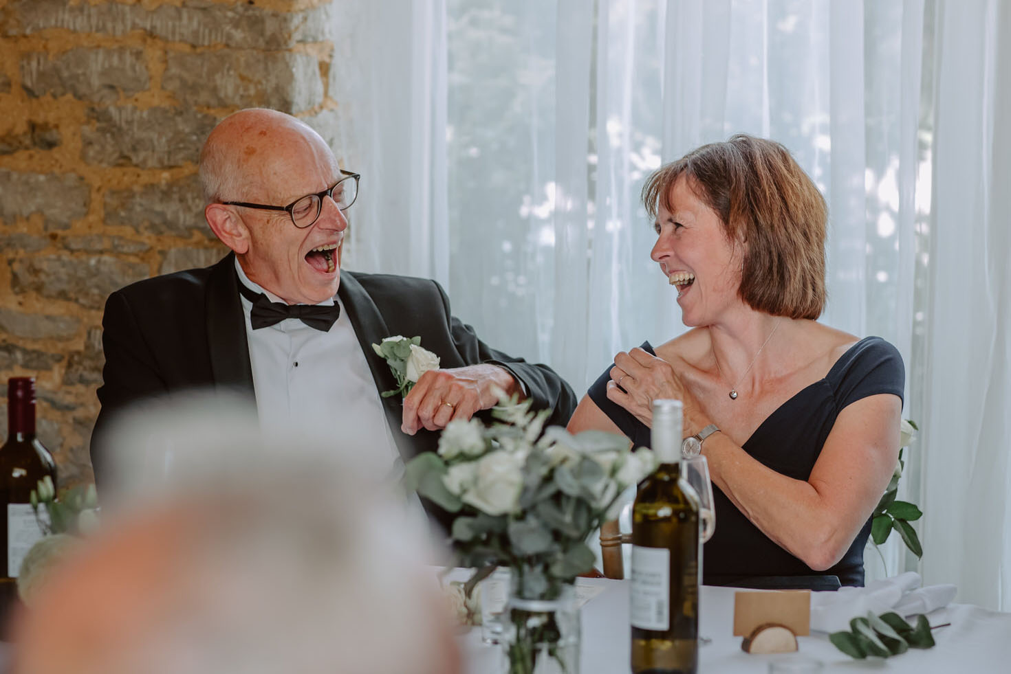 A man and woman laughing at a table at a wedding.