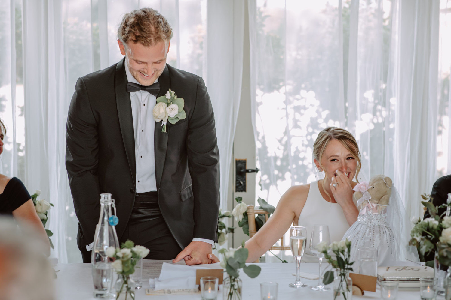A man in a tuxedo sits at a table with a bride and groom.