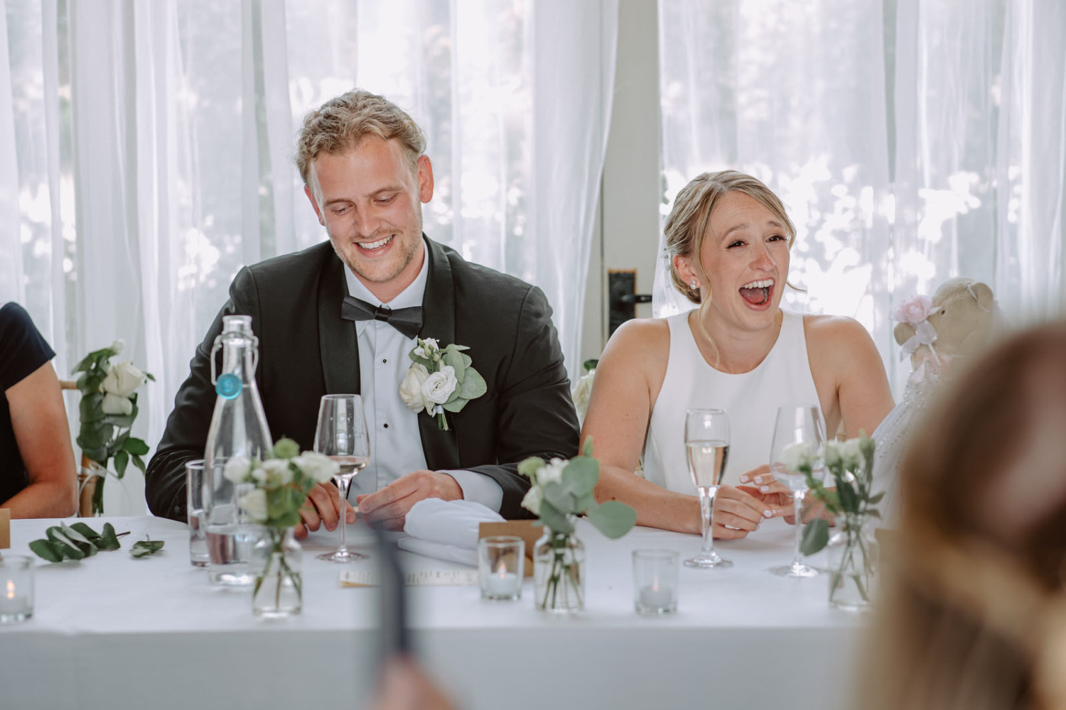 A group of people laughing at a table at a wedding.
