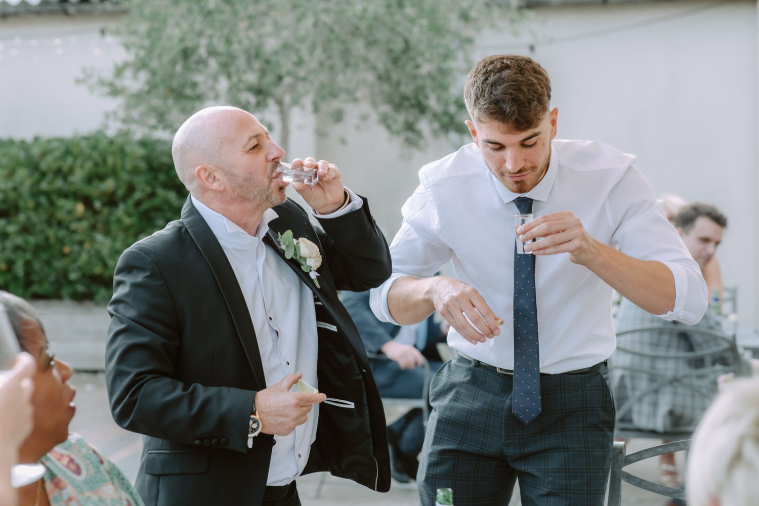 Two men drinking from glasses at a wedding reception.
