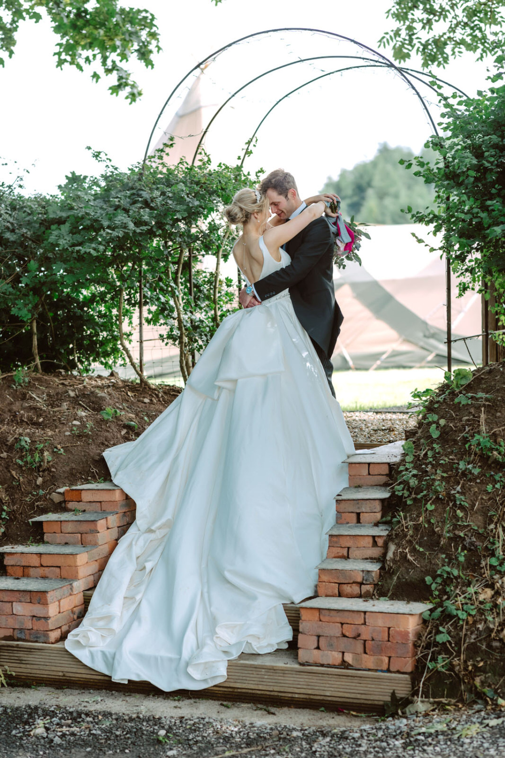 A bride and groom kissing on steps in a garden.