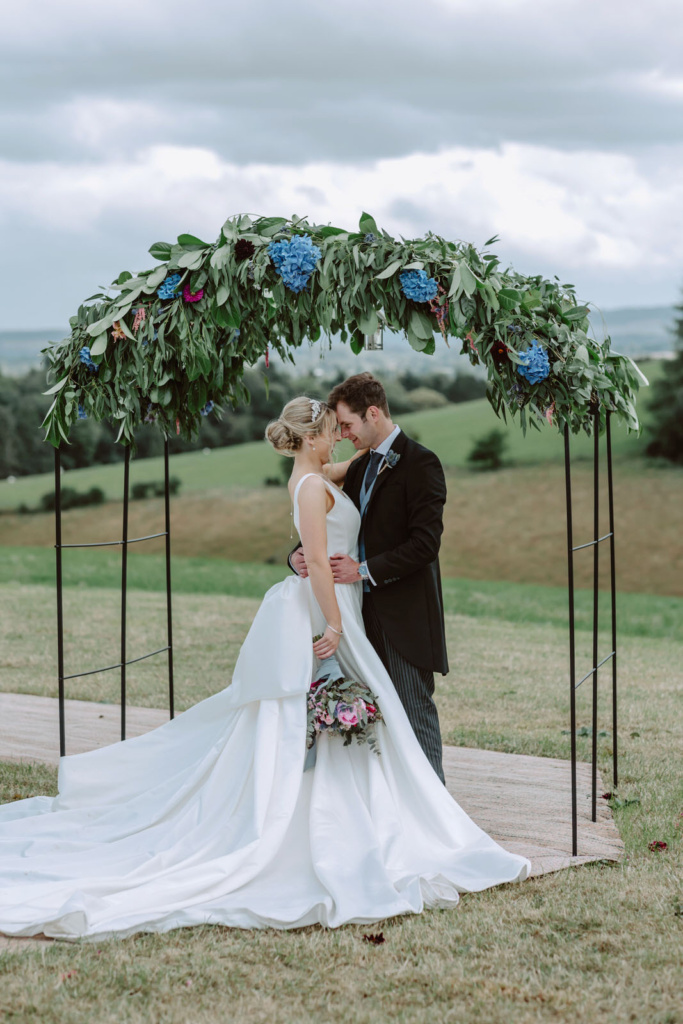 A bride and groom kiss under an arch at their wedding.