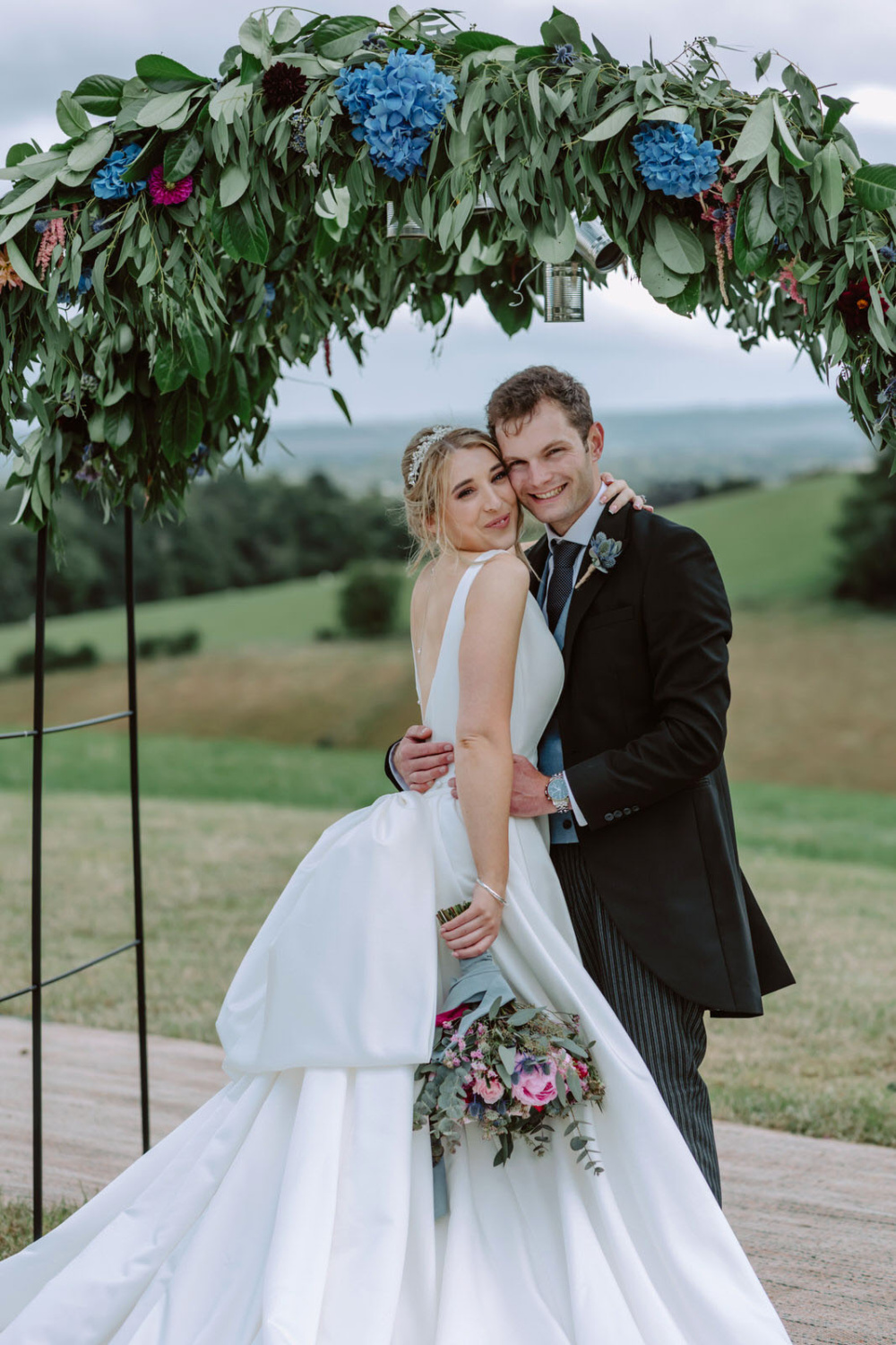 A bride and groom posing in front of a wedding arch.