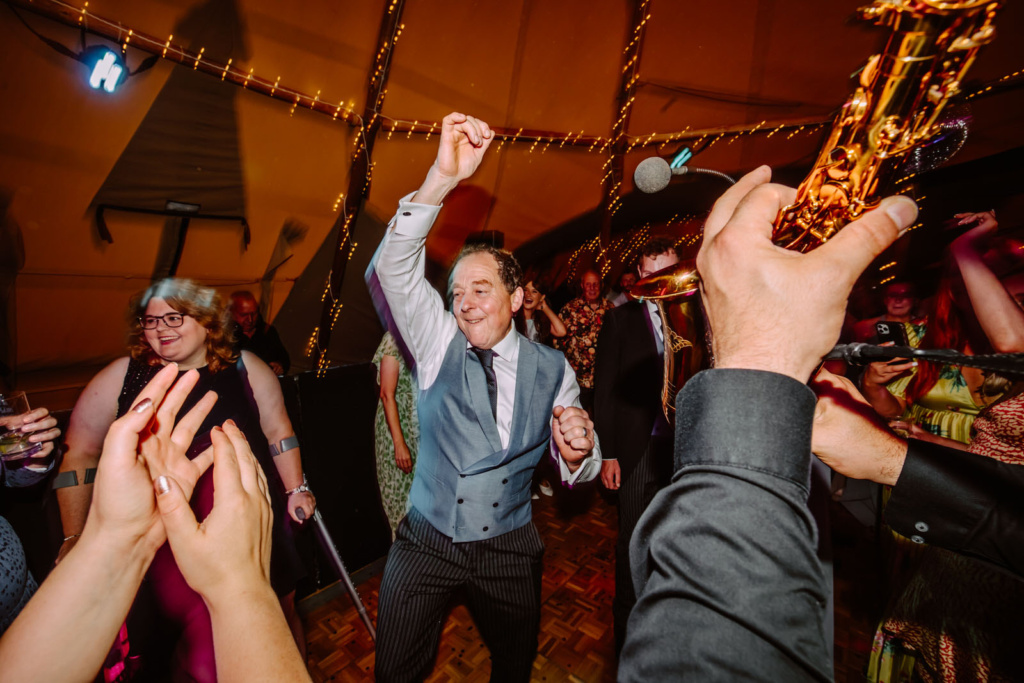 A man is dancing at a wedding reception in a tent.