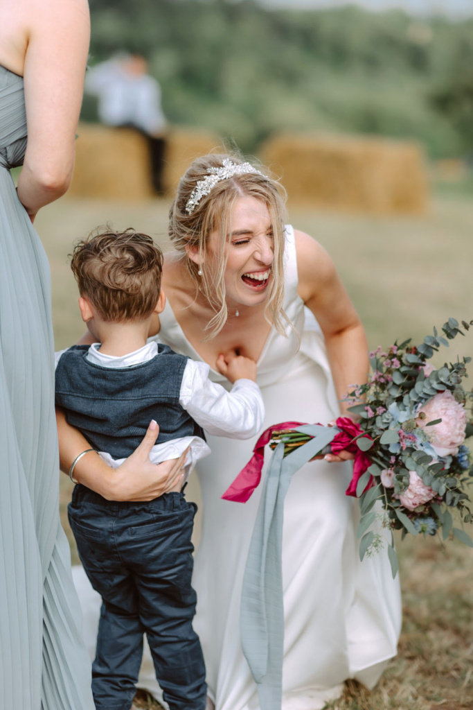 A bride in a wedding dress with a little boy in a field.