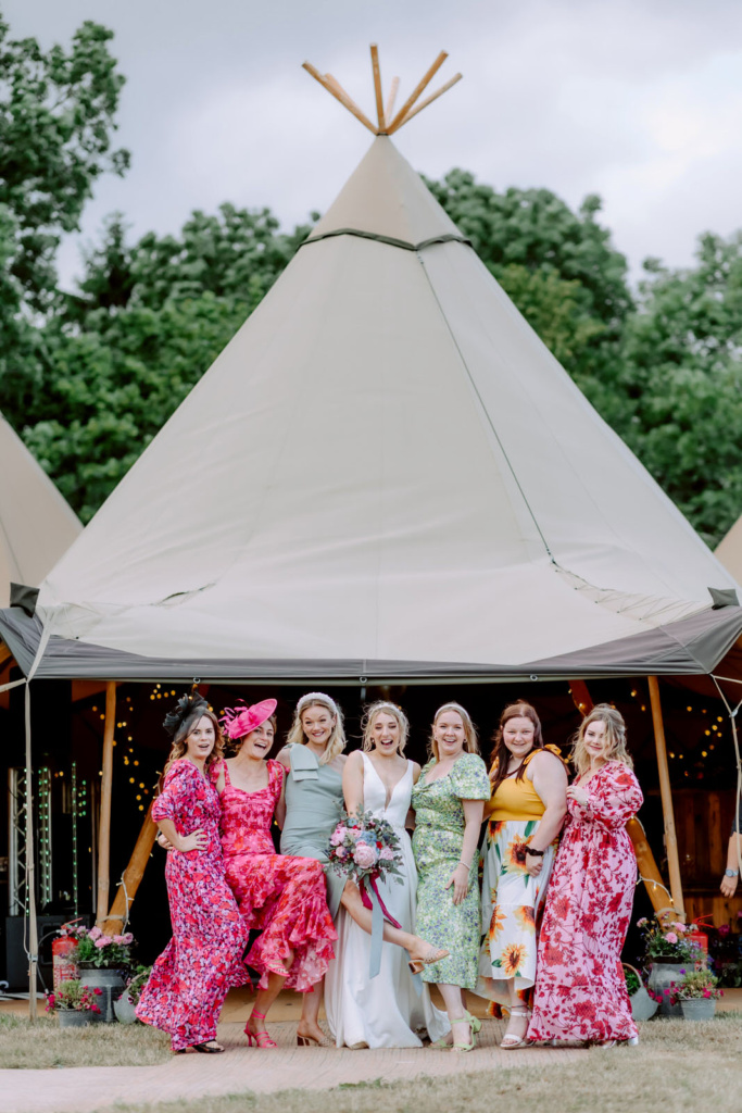 A group of bridesmaids posing in front of a Tipi.