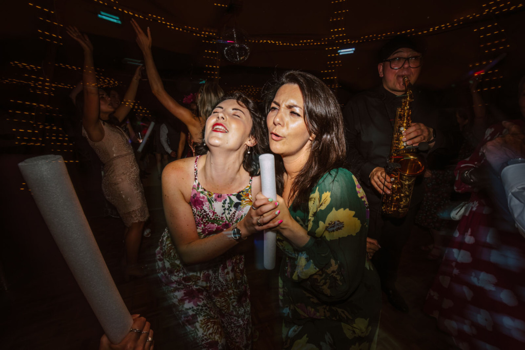 Two women dancing at a party with a saxophone.