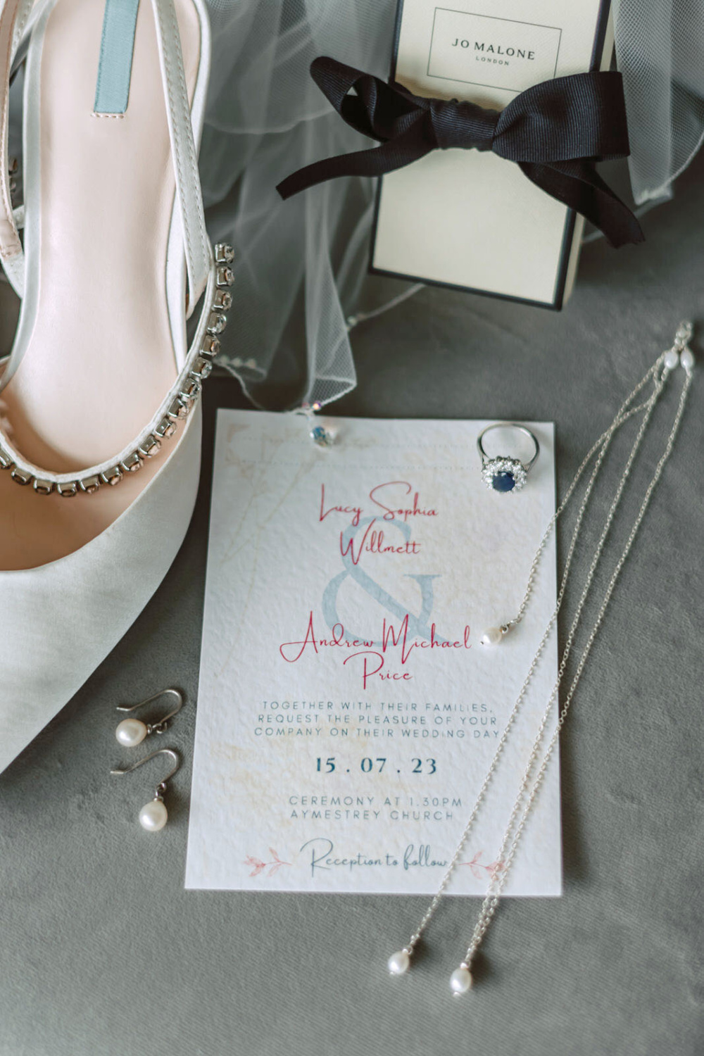 A wedding invitation, wedding shoes and jewelry on a chair.