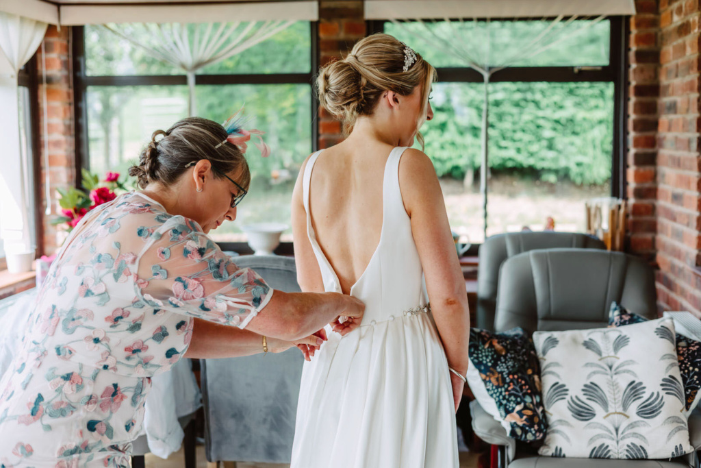 A mother of the bride helping a bride into her wedding dress.