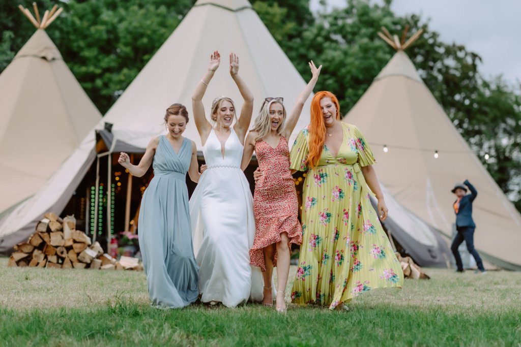 A group of bridesmaids standing in front of a Tipi.