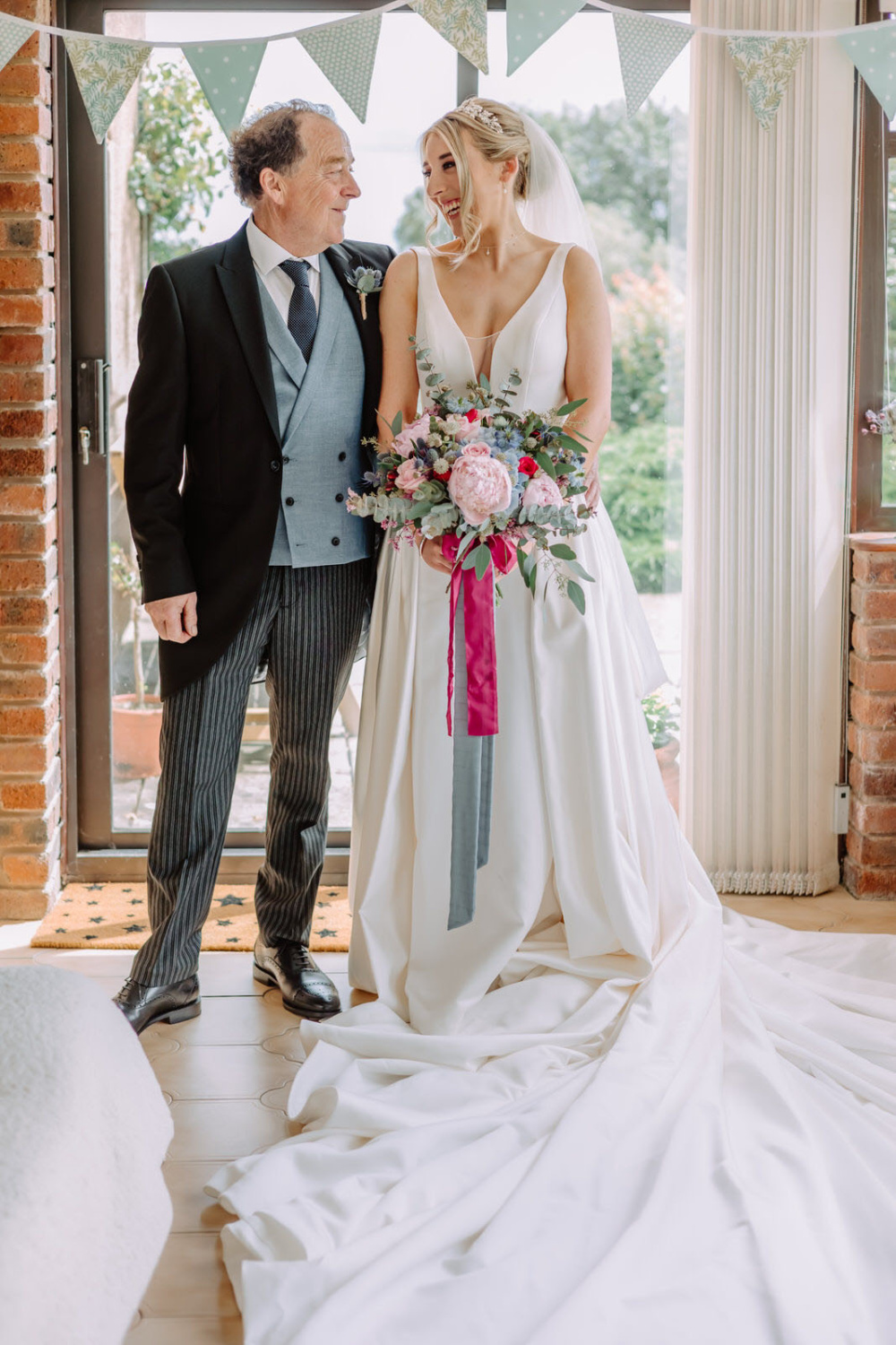 A bride and her dad standing in a room with bunting.