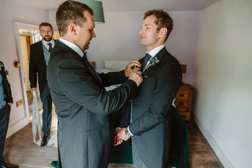 A best man in a suit is adjusting groom's tie.