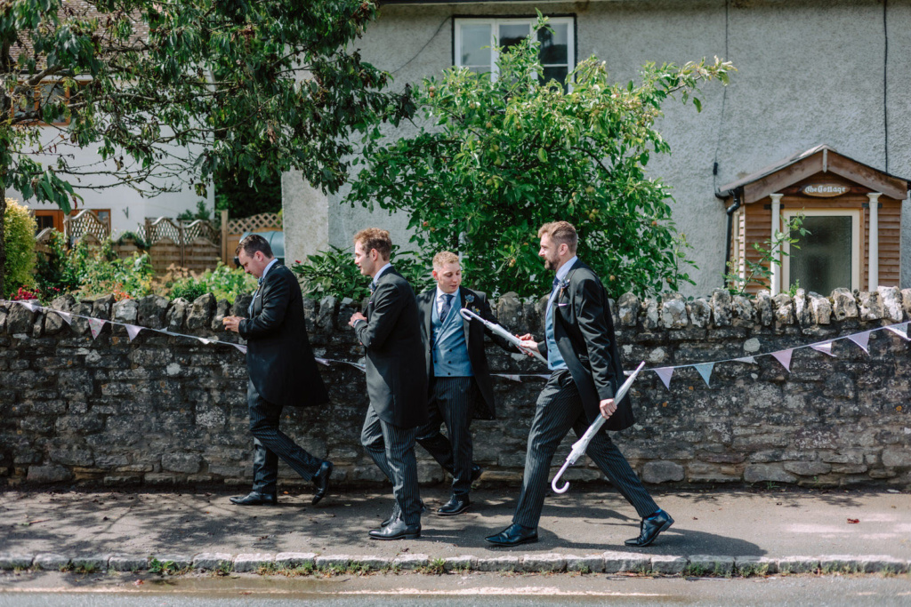 A group of groomsmen in suits walking down a street.