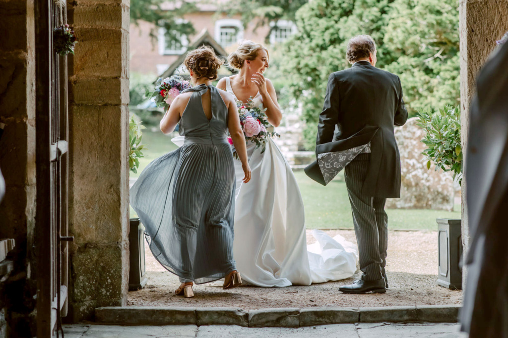 A bride and her bridesmaids are walking out of an archway.