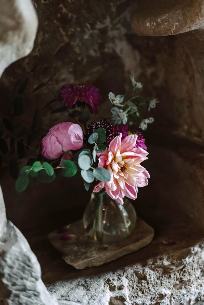 Dahlias in a glass vase in a stone wall.