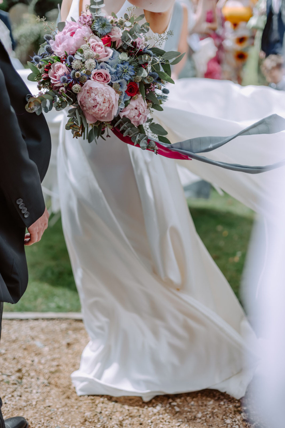 A bride and groom walking down a path with a bouquet.