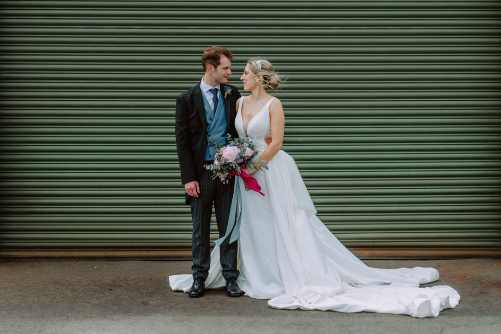 A bride and groom standing in front of a green garage door.