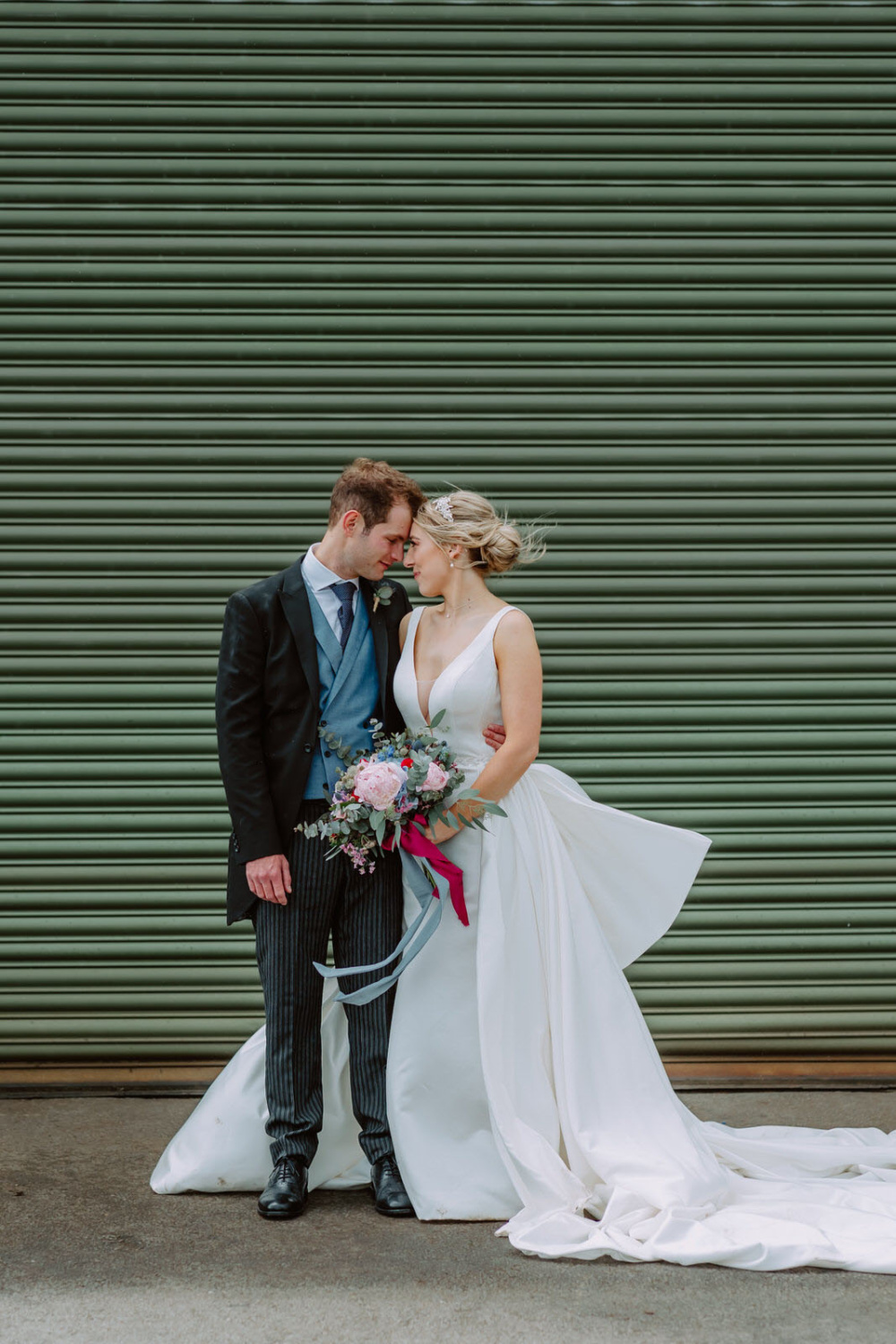 A bride and groom kissing in front of a green garage door.