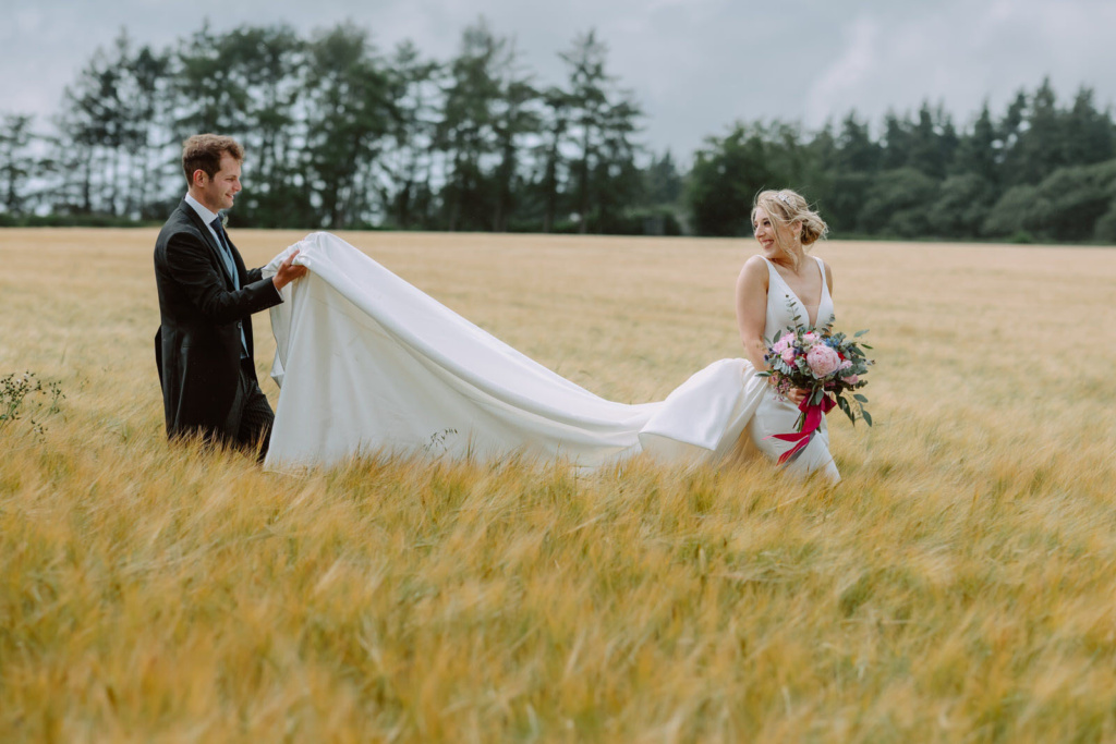 A bride and groom walking through a field of wheat.