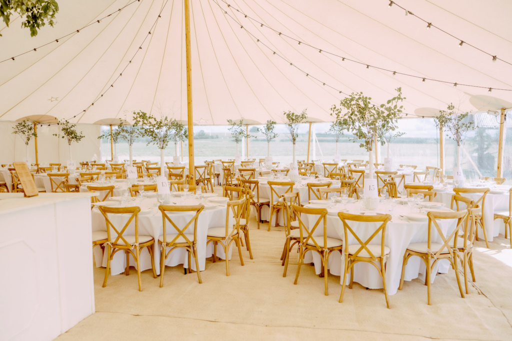 A white marquee with white tables and chairs ready for wedding breakfast.