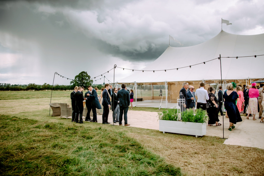 Wedding guests standing in front of a marquee under a stormy sky in Warwickshire farm.