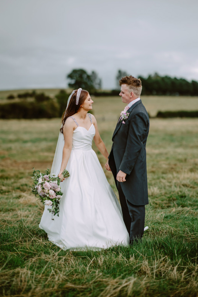 A bride and groom standing together in a field.