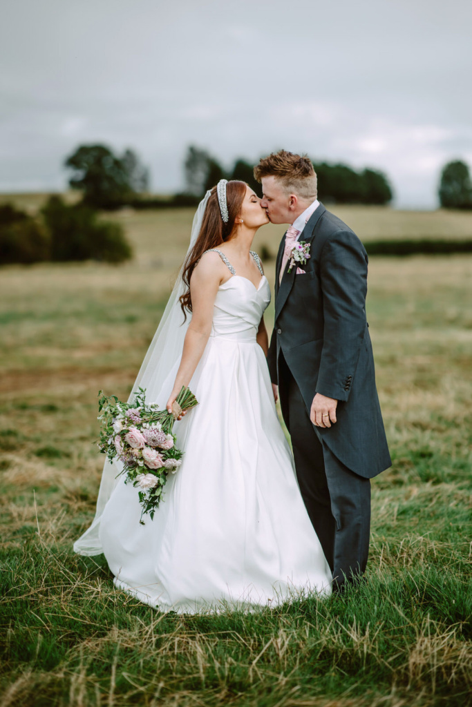 A bride and groom kissing in a field in Warwickshire farm.