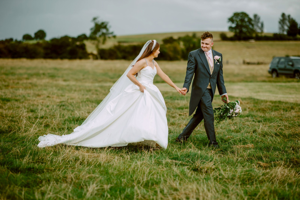 A bride and groom walking through a field at Warwickshire farm.