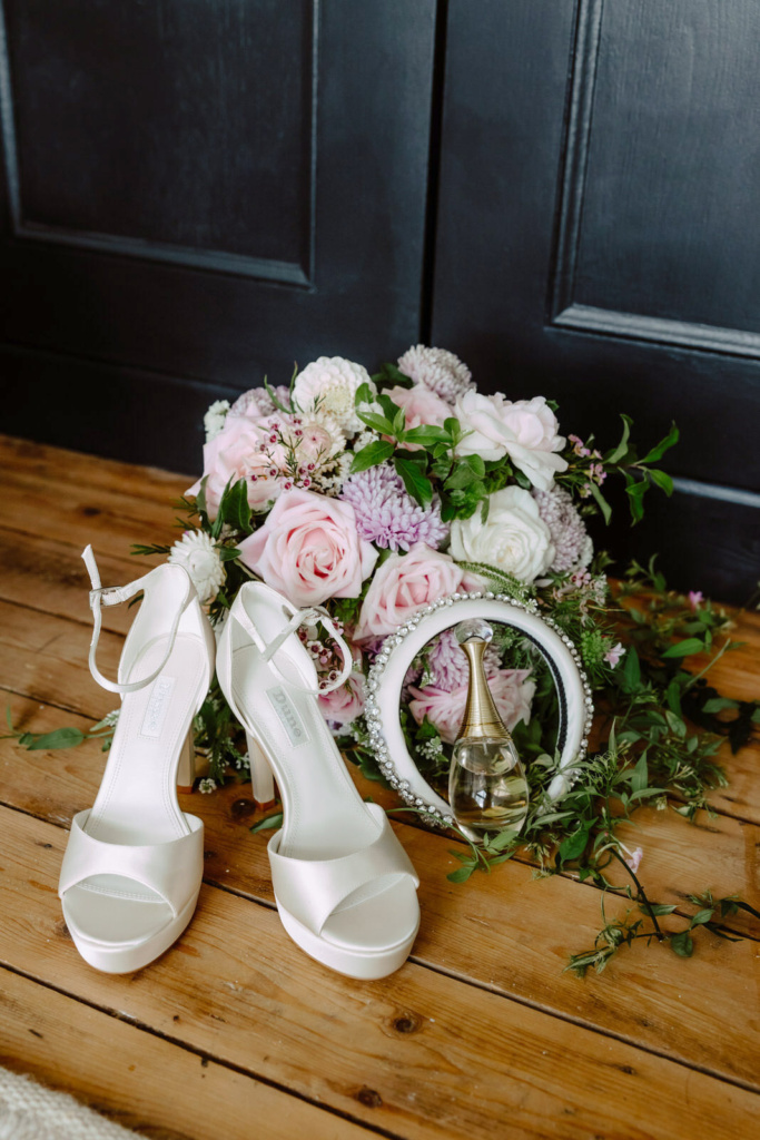 A bouquet of flowers and wedding shoes on a wooden floor.