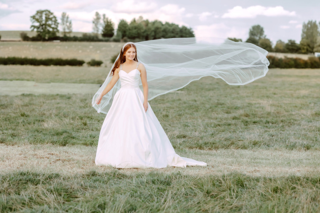 A bride in a field with her veil blowing in the wind.
