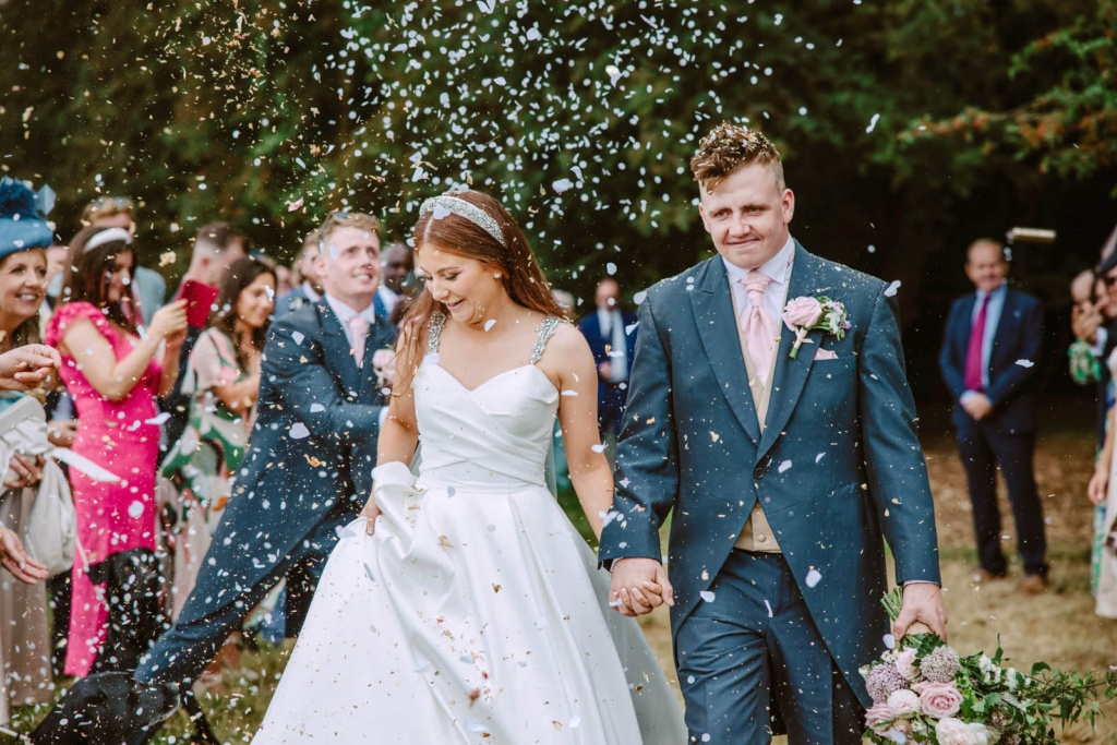 A bride and groom walk down the aisle with confetti thrown at them at Warwickshire Farm.