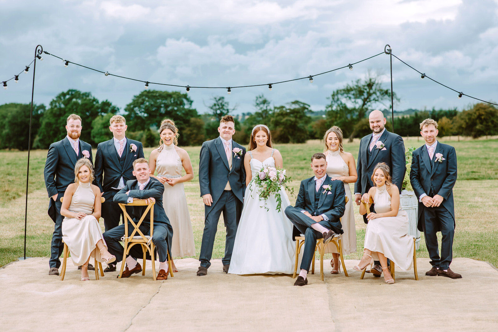 A wedding party posing for a photo in a field at warwickshire farm.