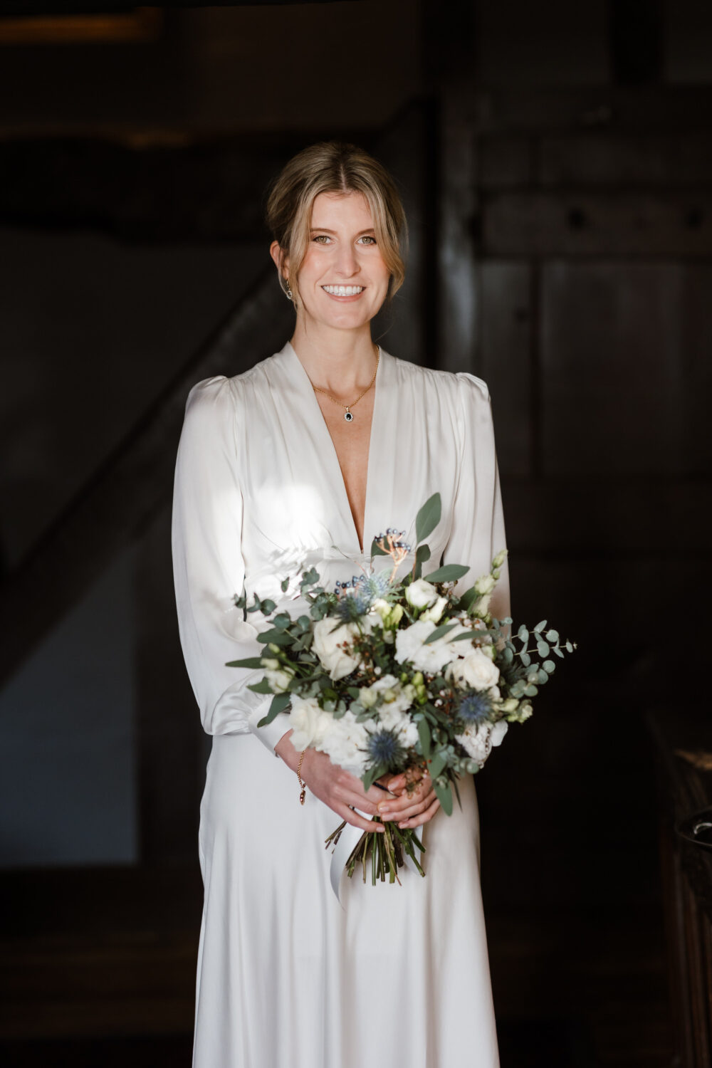 The bride is in a white dress and holding a bouquet of flowers, standing indoors.