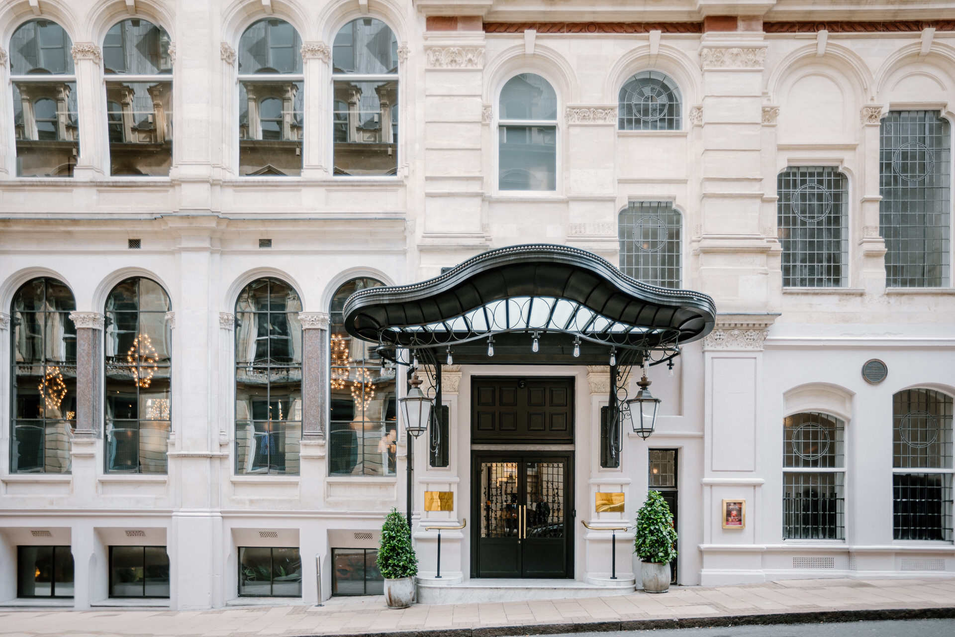 Ornate building The Grand Hotel Birmingham facade with large arched windows, decorative black canopy over entrance, lanterns, and potted plants on either side of the door.