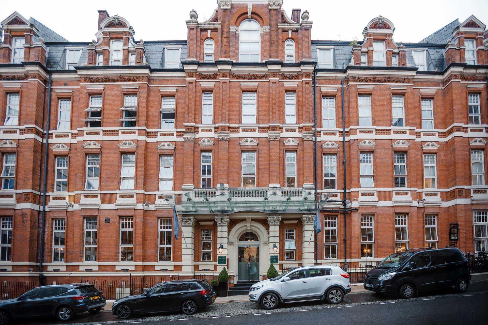 A large, multi-story red-brick building with a decorative entrance, seen from across the street with several parked cars in front. Hotel du vin Birmingham