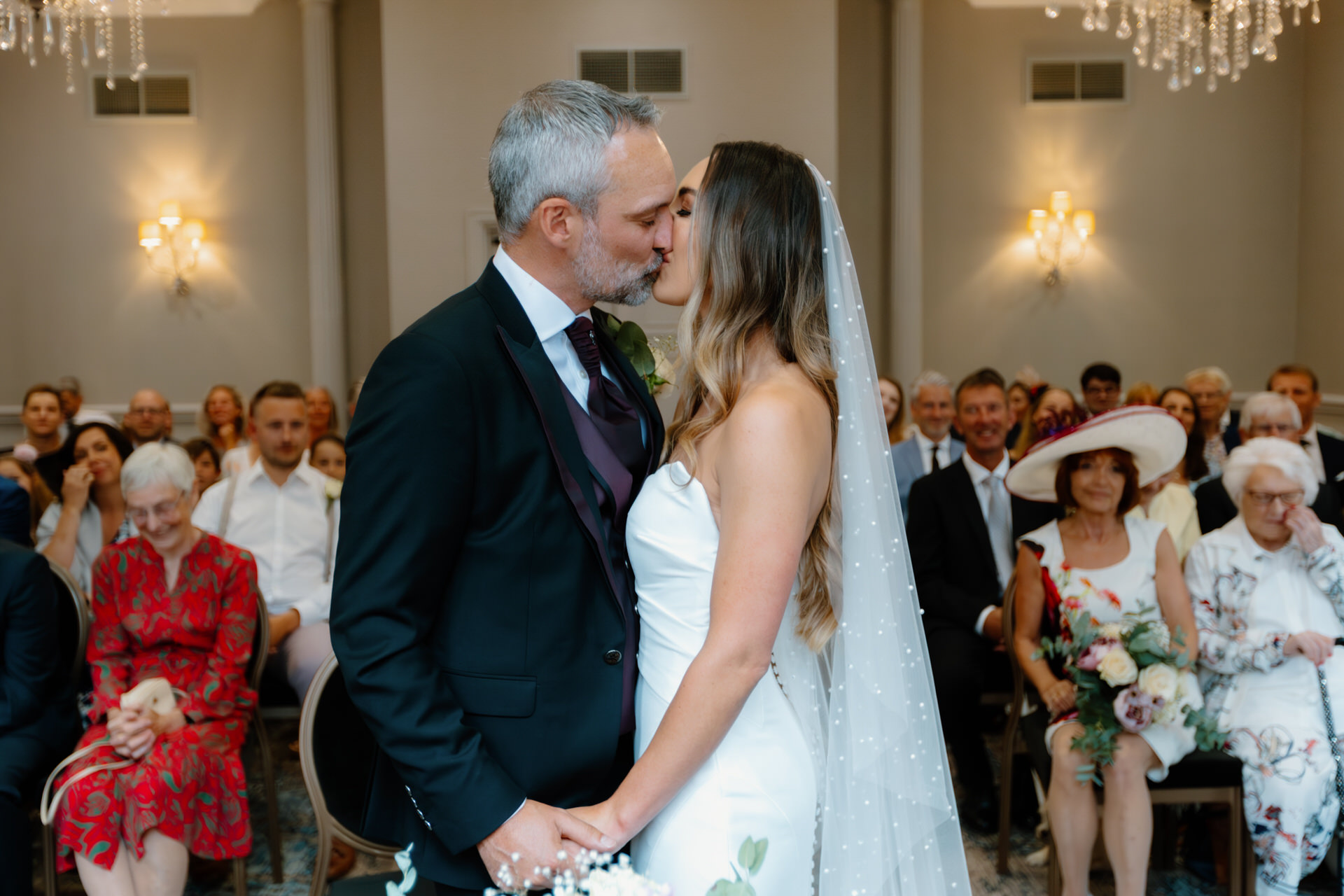 A bride and groom kiss at the altar during their wedding ceremony at Birmingham Hotel du Vin, with guests seated and watching in the background.