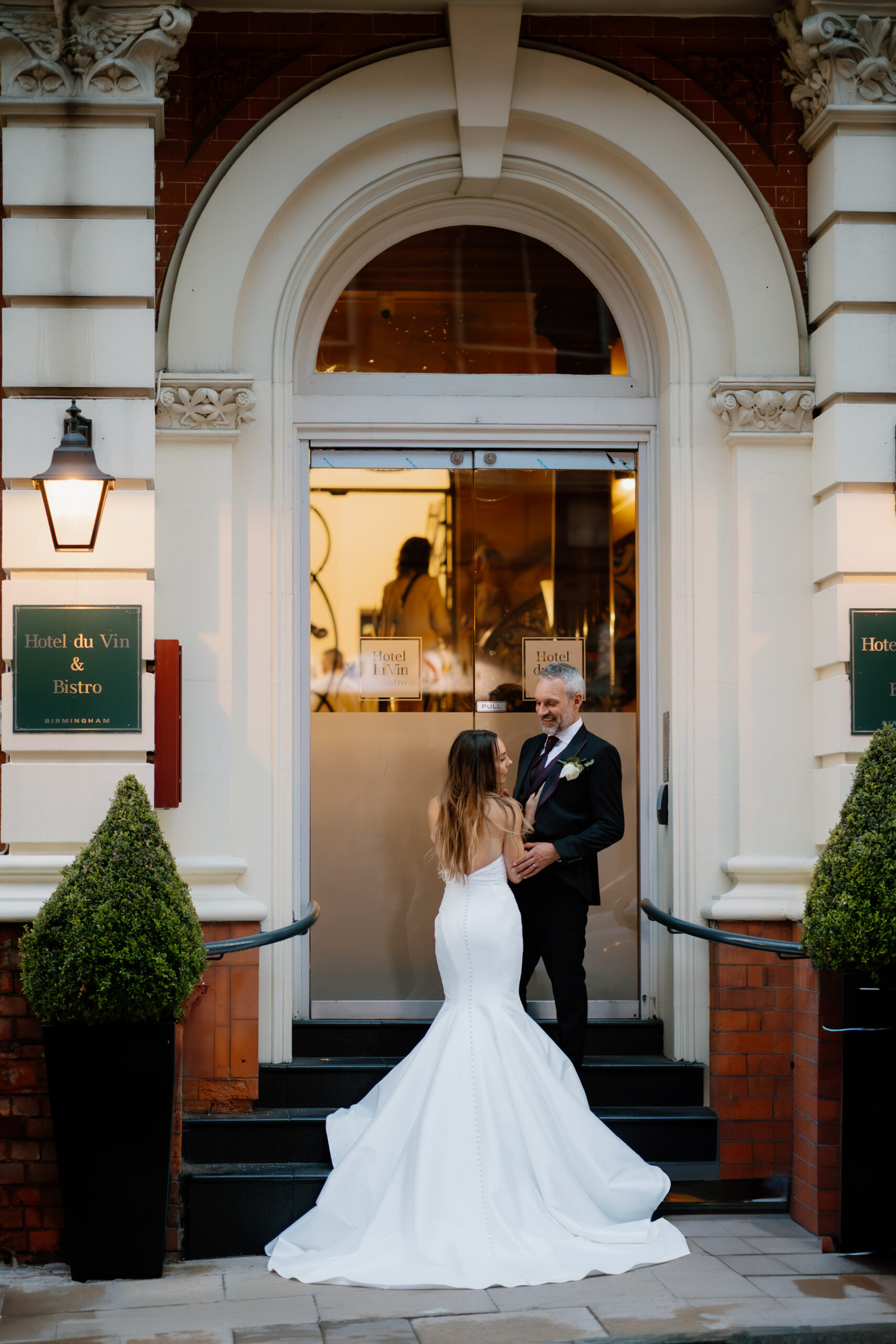 Birmingham Hotel du Vin Wedding Photographer 8 A bride in a white gown and a groom in a black suit stand facing each other on steps outside Hotel du Vin Birmingham, capturing the elegance of their wedding day.