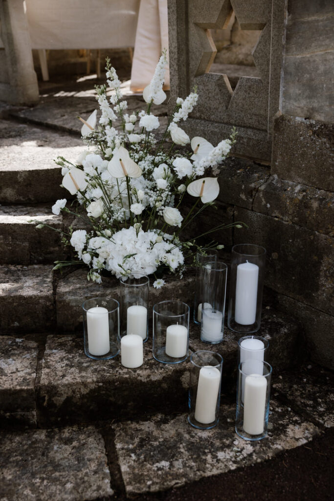 White flowers and large candles arranged on stone steps beside a stone wall with a star-shaped cutout.