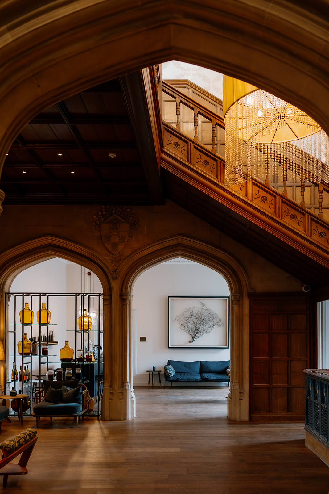 A grand interior featuring arched doorways, a wooden staircase, modern seating, and a large framed artwork on the wall. Warm lighting highlights architectural details.