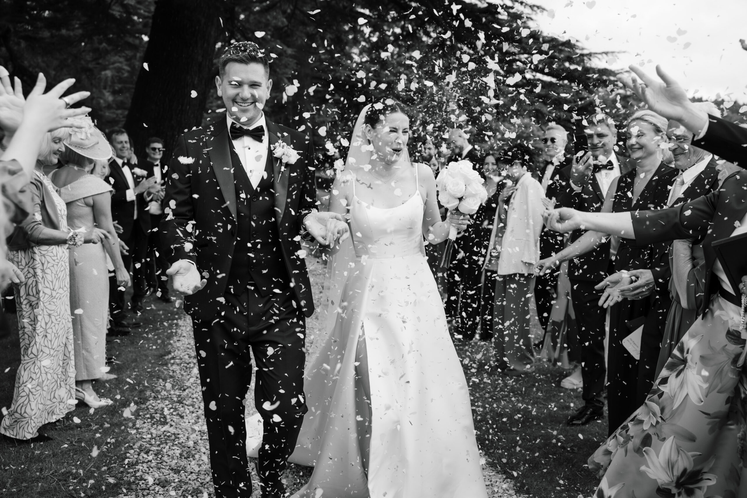 A couple in wedding attire walks hand-in-hand down a path at Broadfield Court, the bride elegantly holding a bouquet of colorful flowers, capturing the essence of perfect wedding photography.