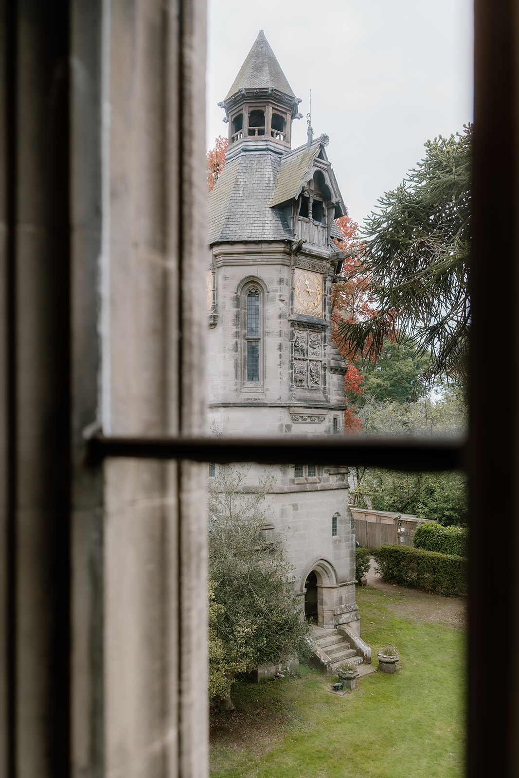 View of the Hampton Manor clock tower with an arched entrance and pointed roof, seen through a window with a horizontal bar in the foreground.