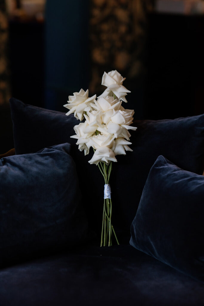 A bouquet of white roses with stems wrapped in white ribbon is placed on a dark, plush velvet cushion.
