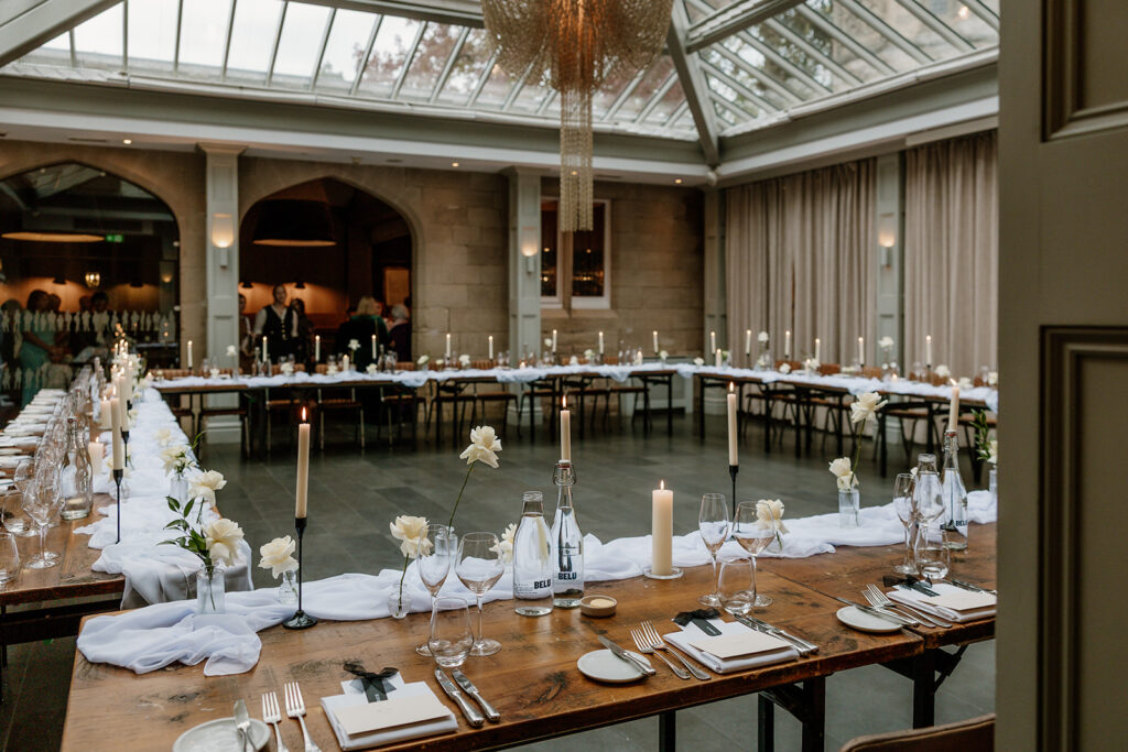A large, elegant dining room set up for an event, with U-shaped tables decorated with white flowers, candles, glassware, and place settings.