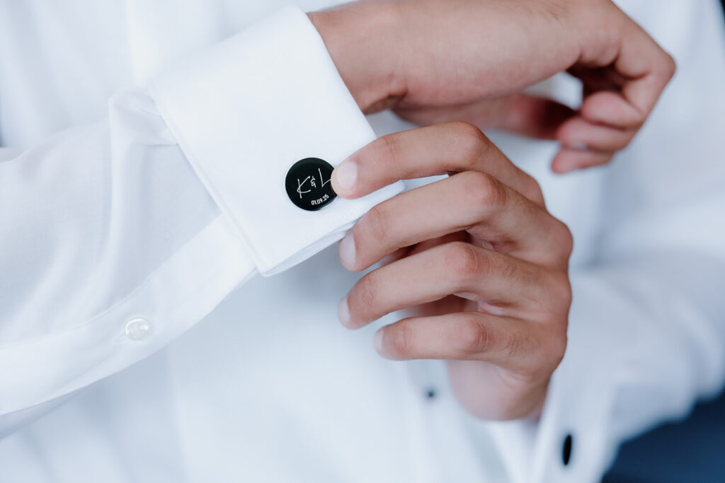A person adjusts a black cufflink on the white sleeve of a dress shirt.